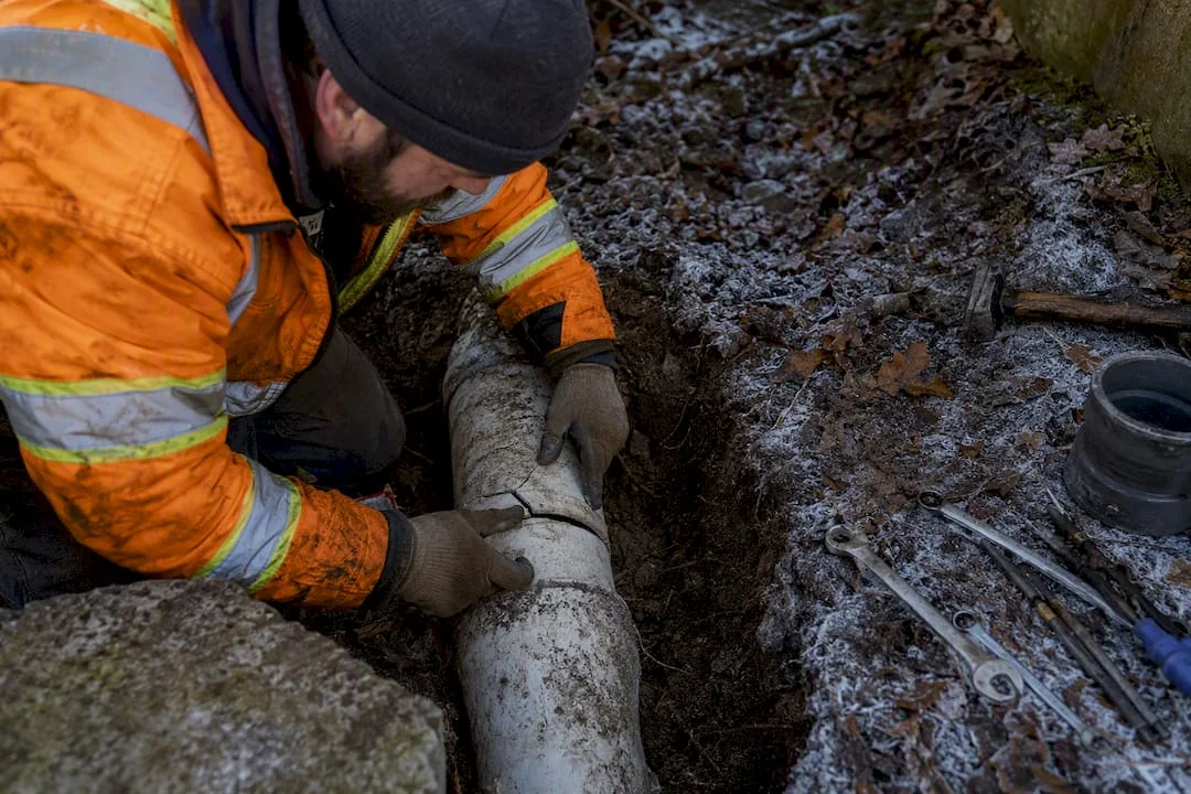 Technician inspecting frost-damaged sewer pipe outdoors